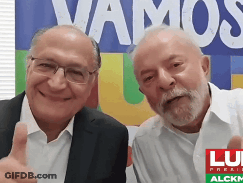 Two Men Posing In Front Of Vamos Sign GIF
