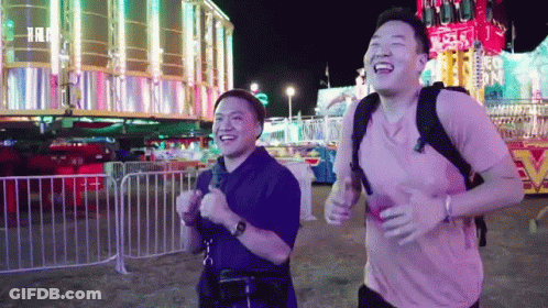 Two Men Running And Laughing Near Carnival Ride GIF