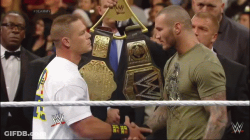 Two Men Shaking Hands In A Wrestling Ring With One Wearing A Shirt That Says ' I Am The One ' On It GIF