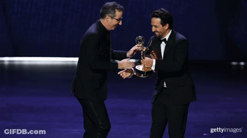 Two Men Shaking Hands On A Stage While One Holds A Trophy GIF