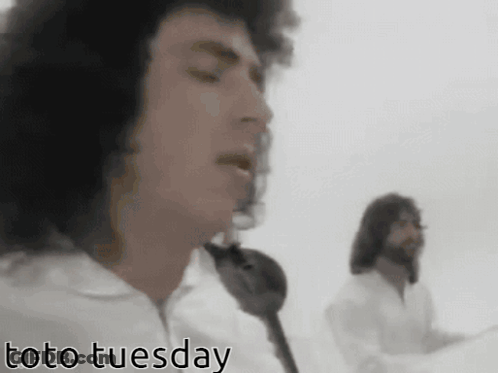 Two Men Singing In Front Of A White Background With Toto Tuesday In The Corner GIF