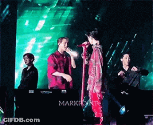 Two Men Singing Into Microphones On Stage With Green Light GIF