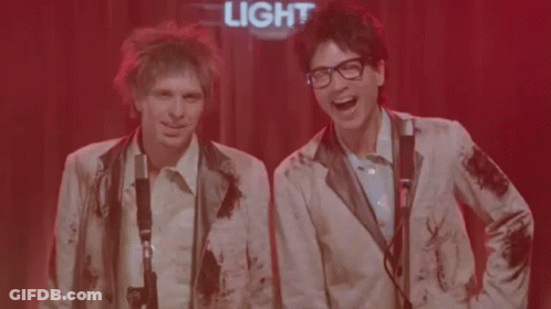 Two Men Singing Into Microphones Under Light Sign GIF