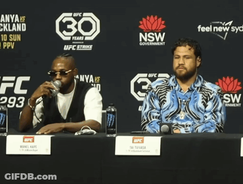 Two Men Sit At A Table In Front Of A Sign That Says 30 GIF