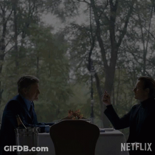 Two Men Sit At A Table With A Bottle Of Champagne And A Bucket Of Ice GIF