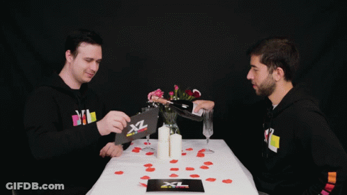 Two Men Sit At A Table With A Card That Says Xl GIF