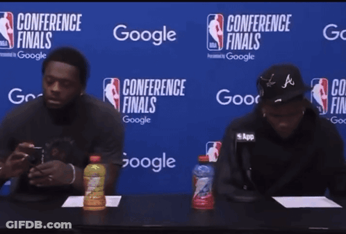 Two Men Sit At Table In Front Of Conference Finals Sign GIF