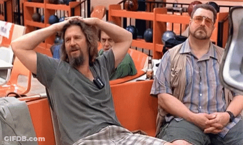 Two Men Sit In A Bowling Alley With Their Hands On Their Head GIF