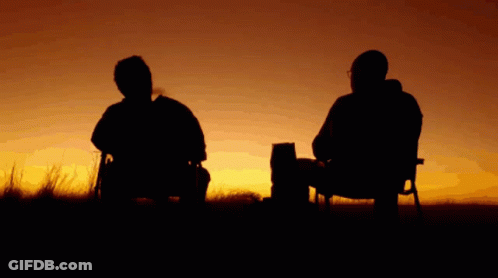 Two Men Sit In Chairs In Front Of A Sunset In A Field GIF