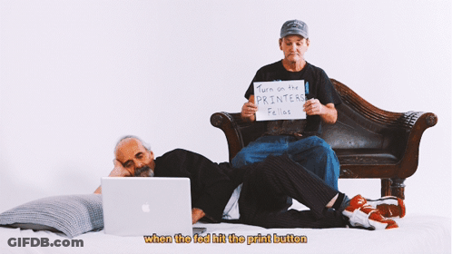 Two Men Sit On A Couch One Holding A Sign That Says Turn On The Printers Fellos GIF