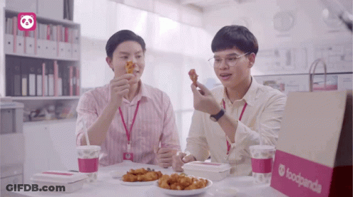 Two Men Sitting At A Table Eating Food From A Foodpanda Bag GIF