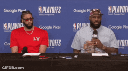 Two Men Sitting At Table In Front Of Google Pixel Sign GIF