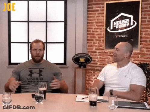 Two Men Sitting At A Table With A Sign That Says House Of Rugby GIF