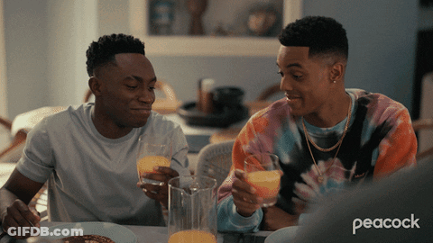 Two Men Sitting At A Table With Peacock Written On The Bottom Left GIF