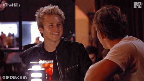 Two Men Sitting At Table With Drink GIF