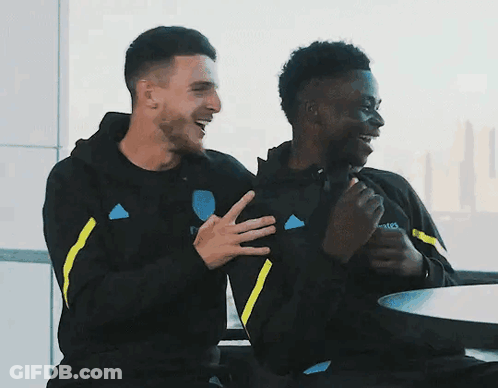 Two Men Sitting At Table With Emirates Sweatshirt GIF