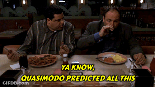 Two Men Sitting At Table With Food And Quasimodo Sign GIF