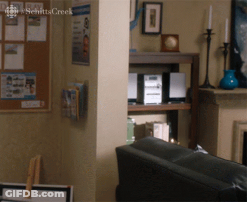 Two Men Sitting At Table With Schitt's Creek Sign GIF