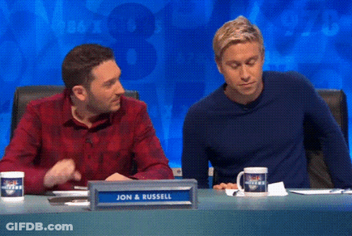 Two Men Sitting At Table With Sign Saying Jon And Russell GIF