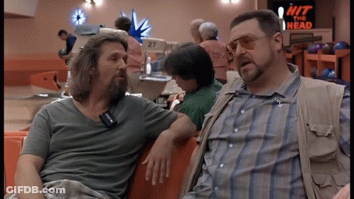 Two Men Sitting In A Bowling Alley With A Sign That Says Hit The Head GIF