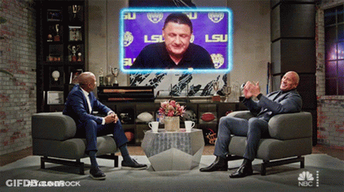 Two Men Sitting In Chairs Before LSU Screen GIF