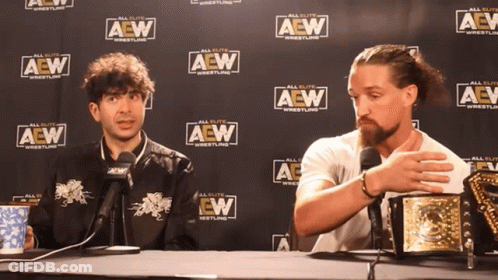 Two Men Sitting In Front Of A Wall That Says Aew Wrestling GIF