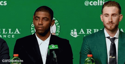 Two Men Sitting In Front Of Green Wall With Celtics GIF