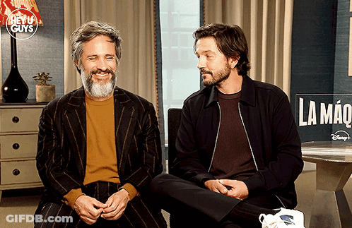 Two Men Sitting In Front Of La Mano Sign GIF
