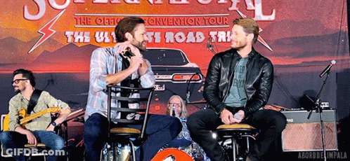 Two Men Sitting In Front Of The Ultimate Road Trip Sign GIF
