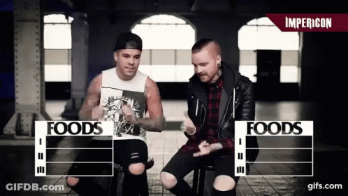 Two Men Sitting Next To Foods Sign GIF