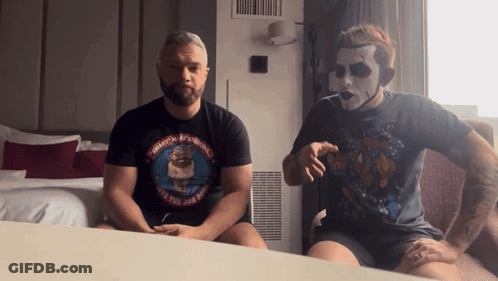 Two Men Sitting On A Bed With One Wearing A Shirt That Says ' Masters Of The Universe ' On The Front GIF