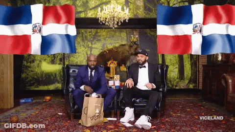 Two Men Sitting On A Couch With A Bag That Says City Market GIF