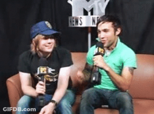 Two Men Sitting On A Couch With Microphones In Front Of A Sign That Says News GIF