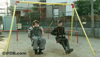 Two Men Sitting On A Swing Set In A Park GIF
