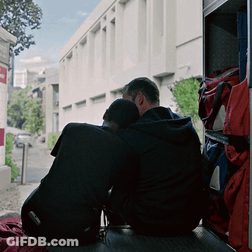 Two Men Sitting On Ambulance Heads Together GIF