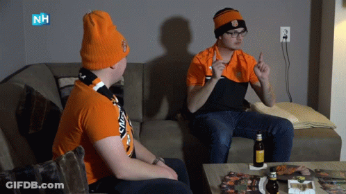 Two Men Sitting On Couch One With NH Logo Shirt GIF