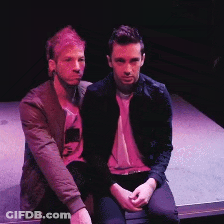 Two Men Sitting On Stage In Dark Room GIF