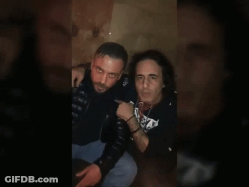Two Men Sitting, One In S.A. Shirt GIF