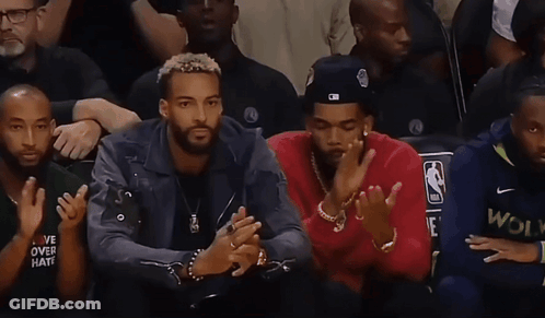 Two Men Sitting, One Wearing NBA Hat GIF