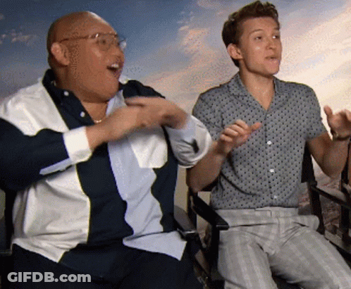 Two Men Sitting With Arms Outstretched One Wearing Glasses GIF