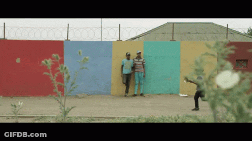 Two Men Stand In Front Of A Colorful Wall With Barbed Wire GIF