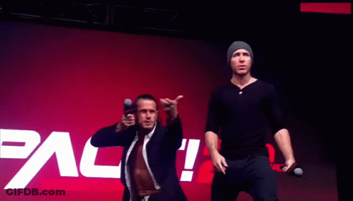 Two Men Stand In Front Of A Pac Wrestling Logo GIF