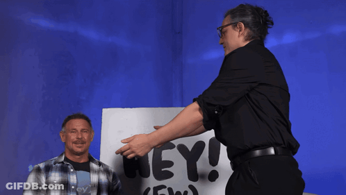 Two Men Stand In Front Of A Sign That Says Aew Hey GIF