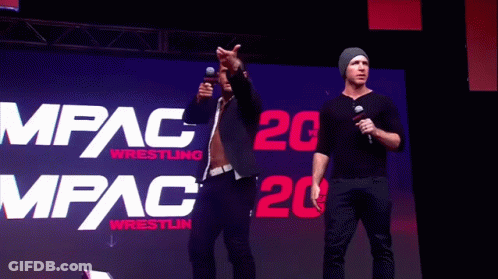 Two Men Stand On A Stage With Microphones In Front Of A Mpac Wrestling Sign GIF