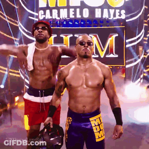 Two Men Standing Before Carmelo Hayes Sign GIF