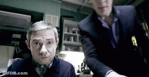 Two Men Standing In Dark Room One Looking At Camera GIF