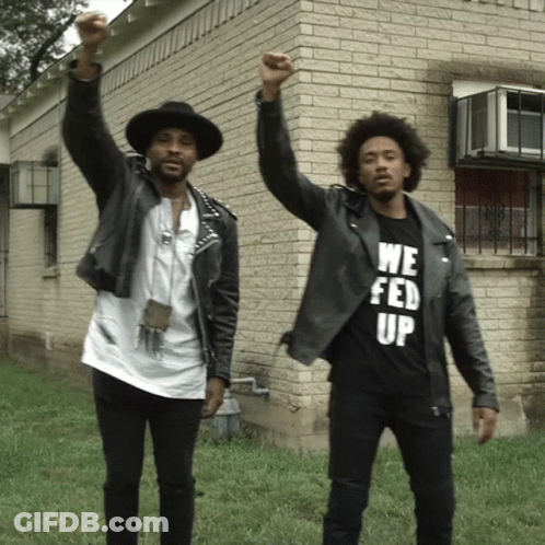 Two Men Standing In Front Of A Brick Building One Wearing A We Fed Up T-Shirt GIF