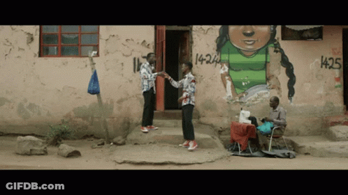 Two Men Standing In Front Of A Building With Graffiti On It That Says 1425 GIF