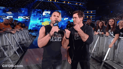 Two Men Standing In Front Of A Crowd With One Wearing A Shirt That Says Among GIF