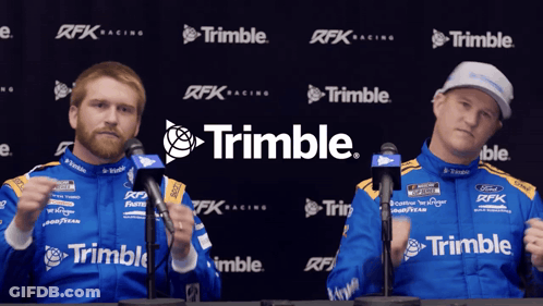 Two Men Standing In Front Of A Trimble Banner GIF